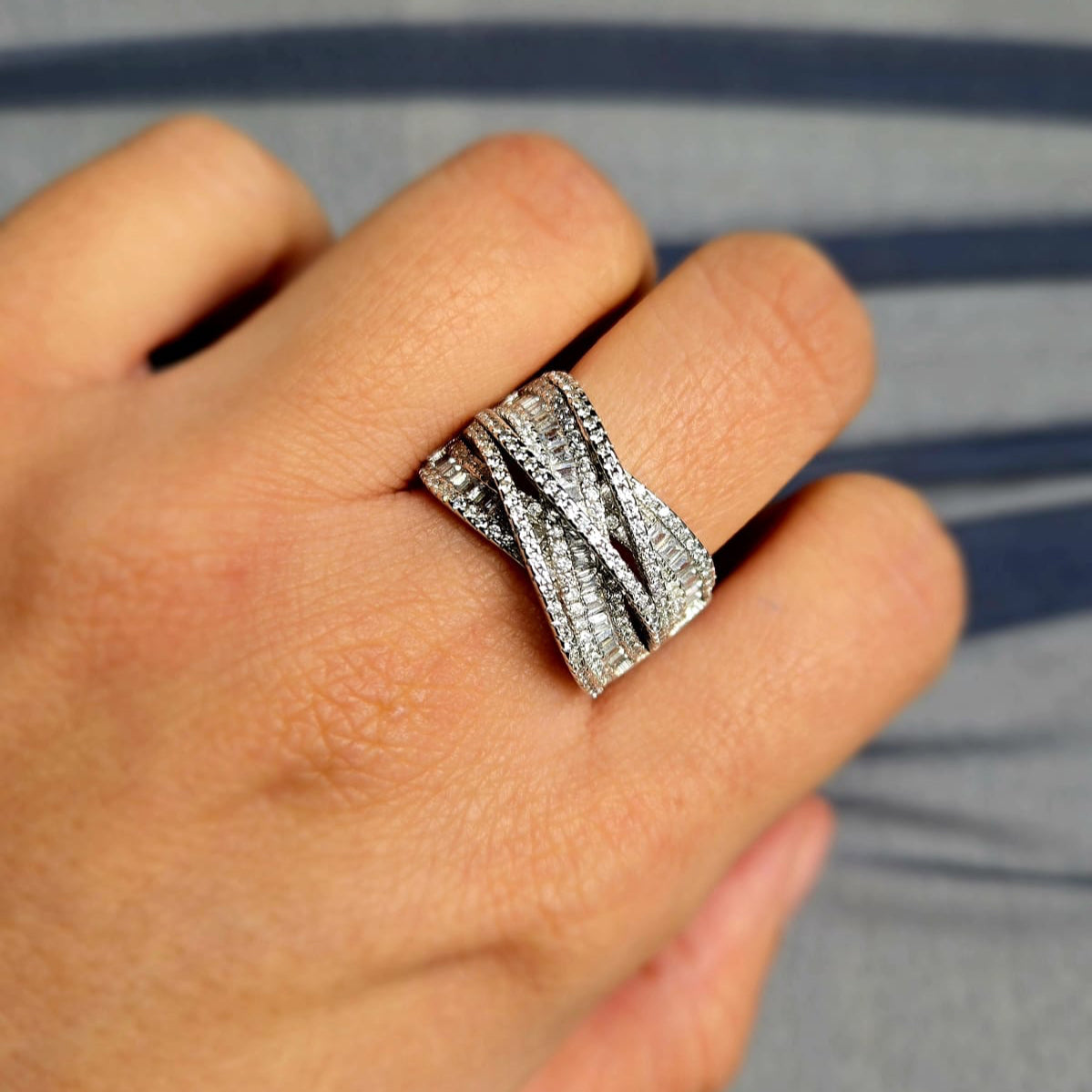 Silver ring with gemstones on a person's finger against a neutral background