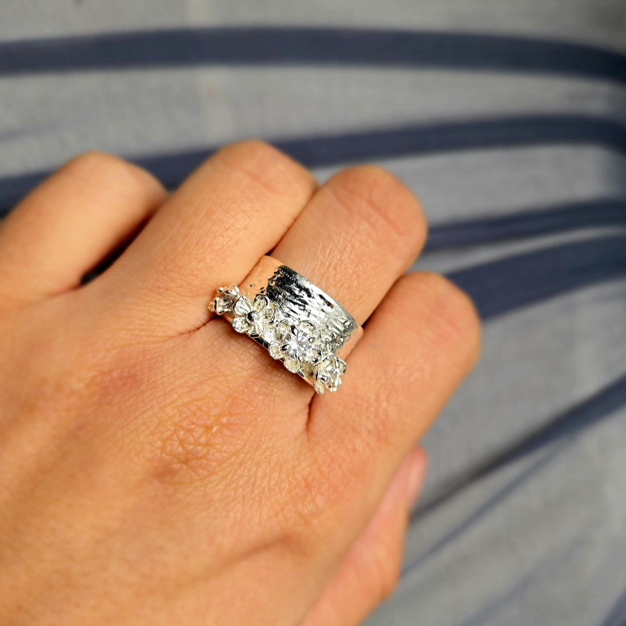 Hand wearing a silver ring with multiple diamonds against a blurred background