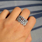 Silver ring with gemstones on a finger against a gray background