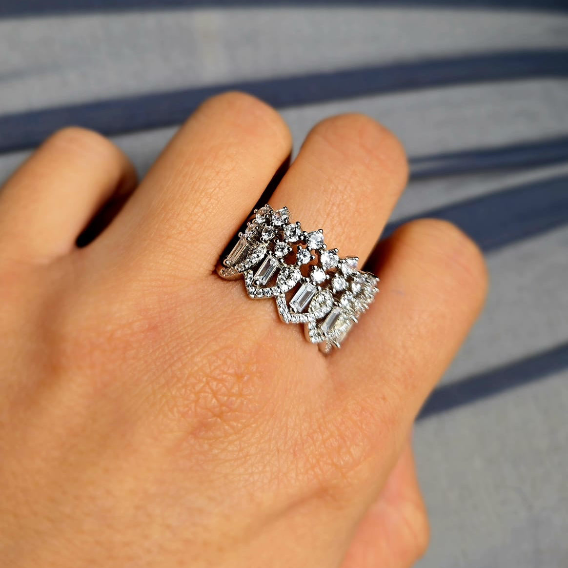 Silver ring with gemstones on a finger against a gray background