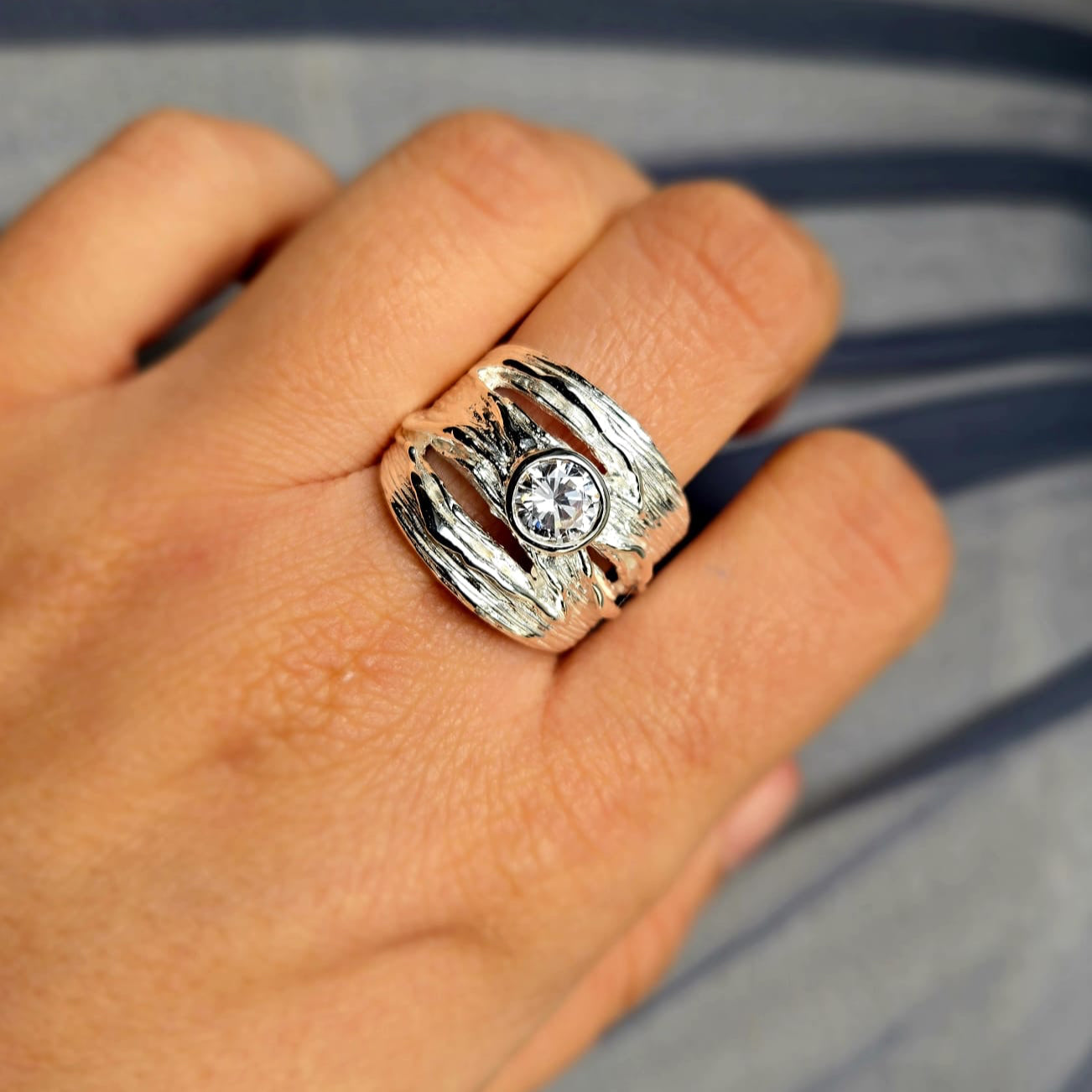 Silver ring with a diamond on a person's finger against a blurred background