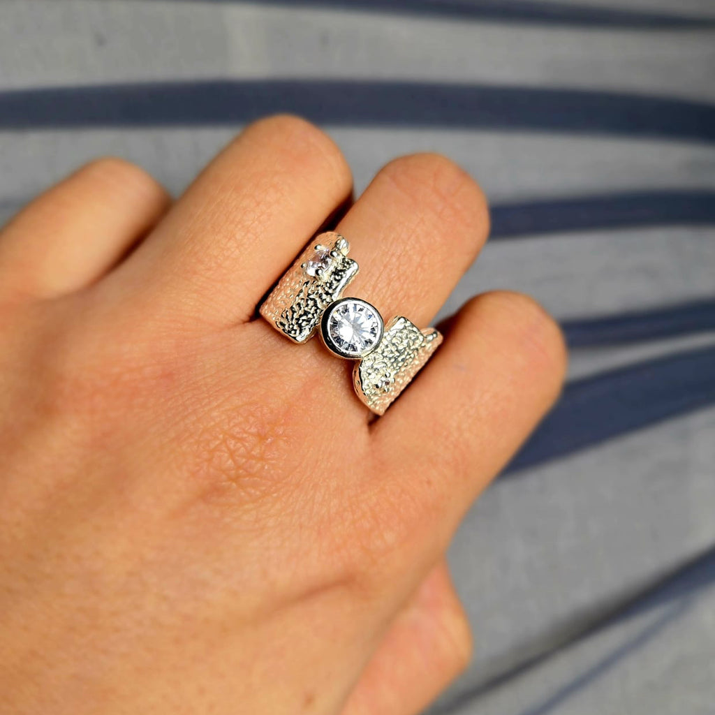 Close-up of a hand wearing two silver rings with a clear gemstone on a striped background