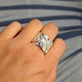 Silver ring with a diamond on a person's finger against a striped background