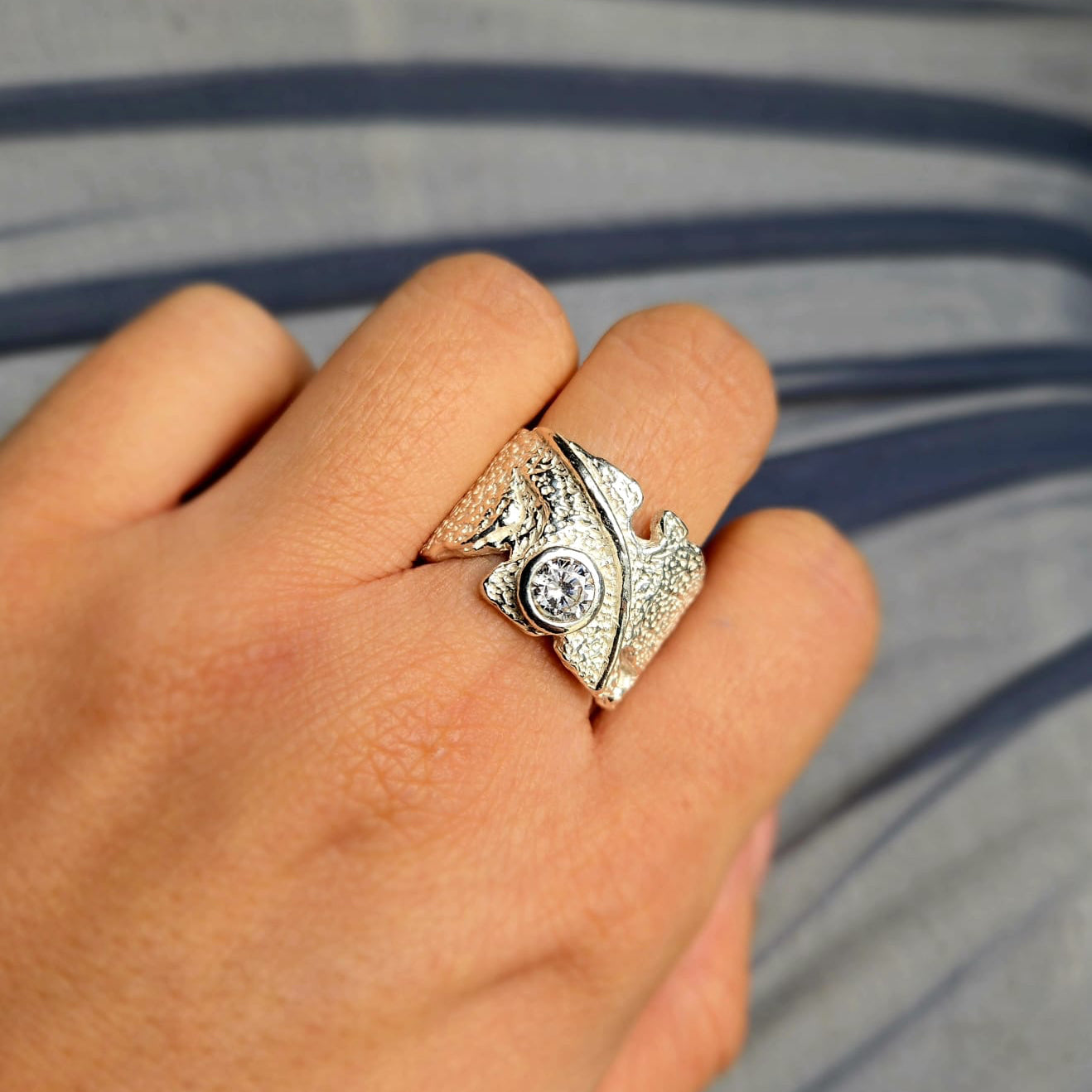 Silver ring with a diamond on a person's finger against a striped background