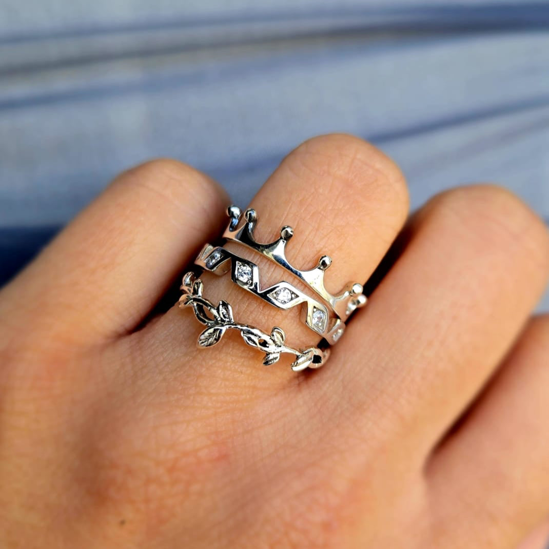 Silver ring with a crown design on a person's finger against a blurred background