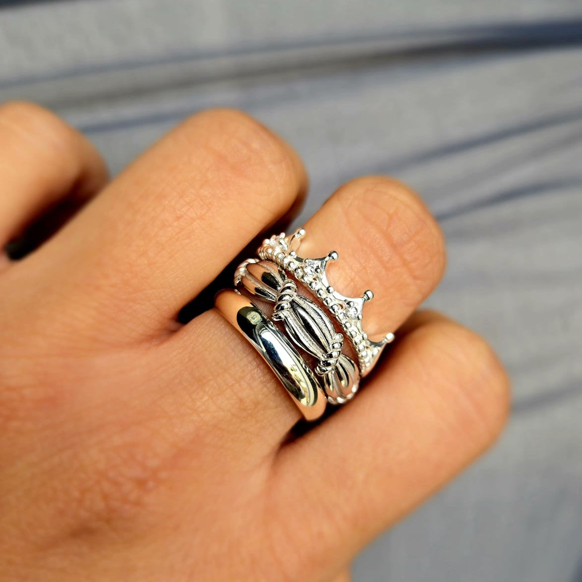 Hand wearing a silver ring with a crown design on a blurred background