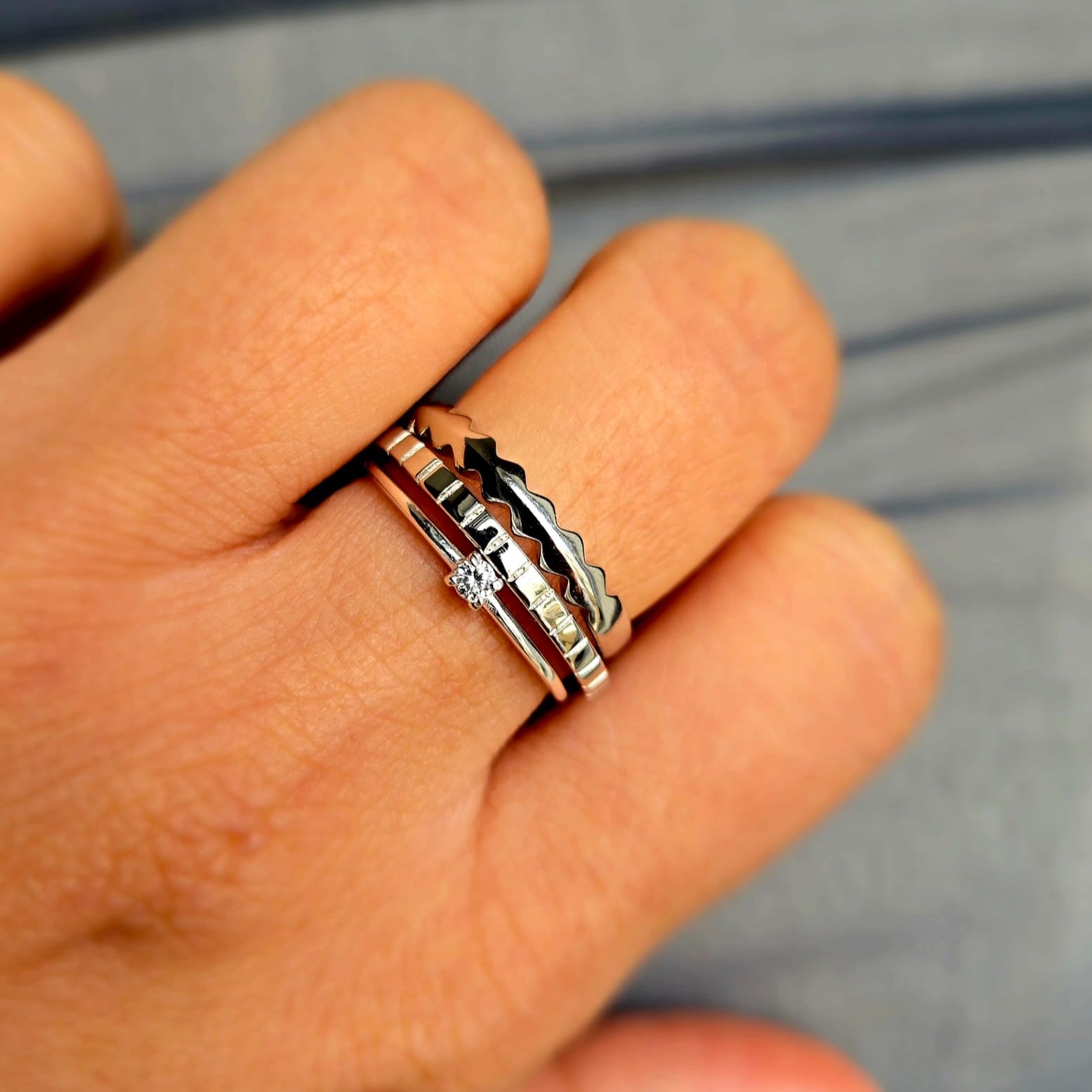 Silver ring with a diamond on a person's finger against a blurred background