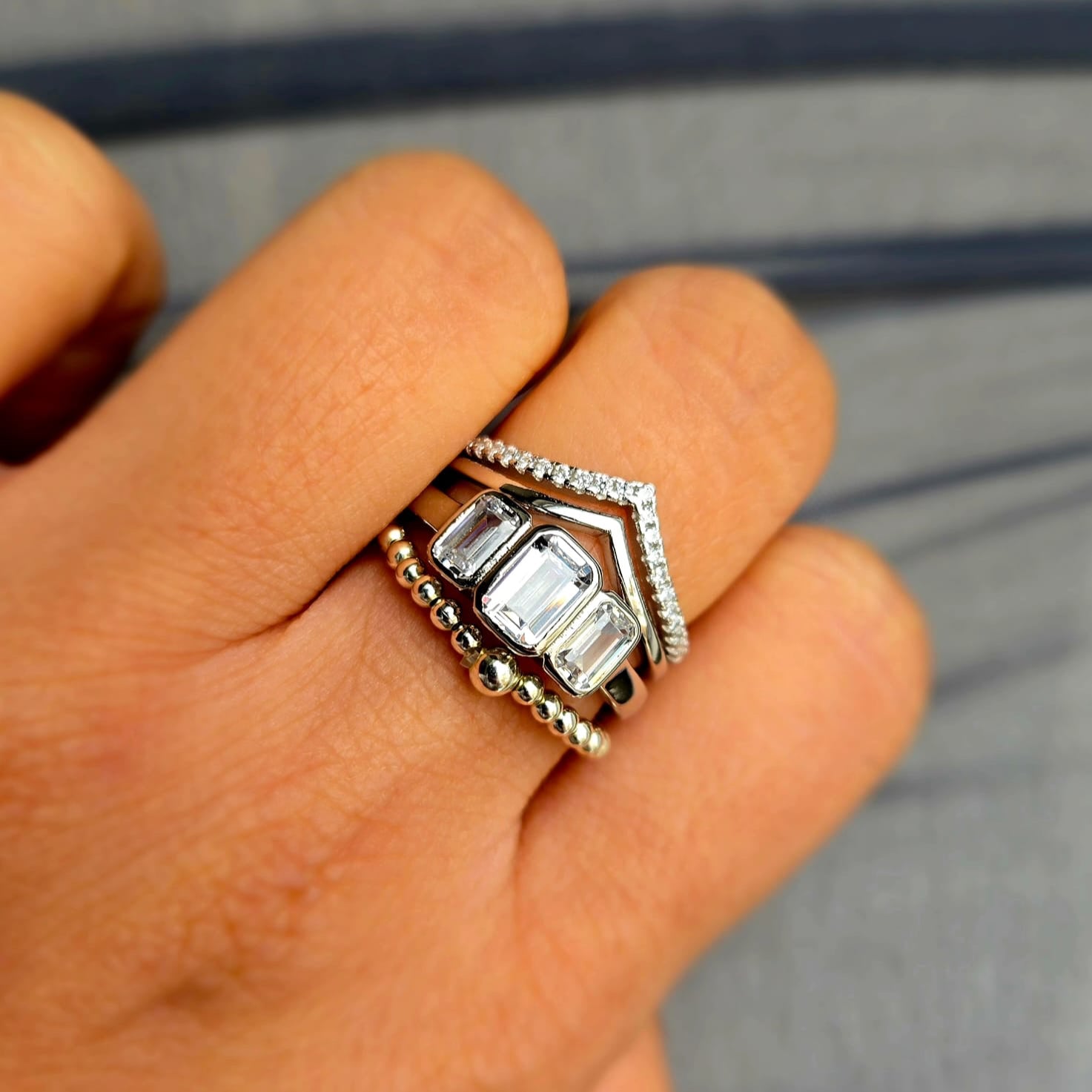 Close-up of a hand wearing two silver rings with gemstones on a neutral background