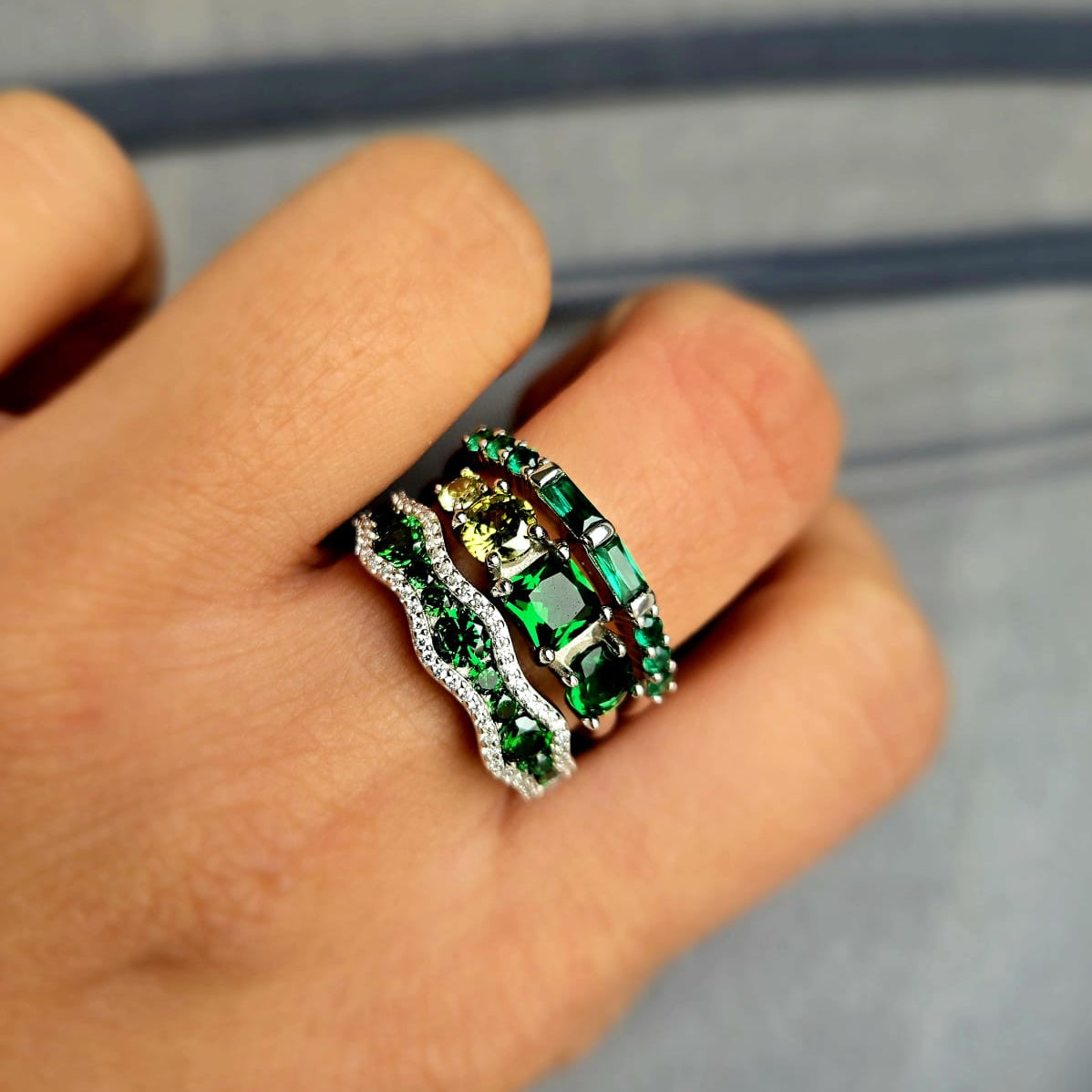 Close-up of a hand wearing a green gemstone ring with a blurred background