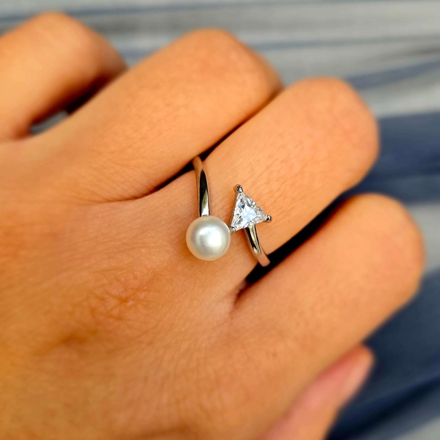 Two rings on a person's finger: one with a pearl and the other with a triangle-shaped gemstone.