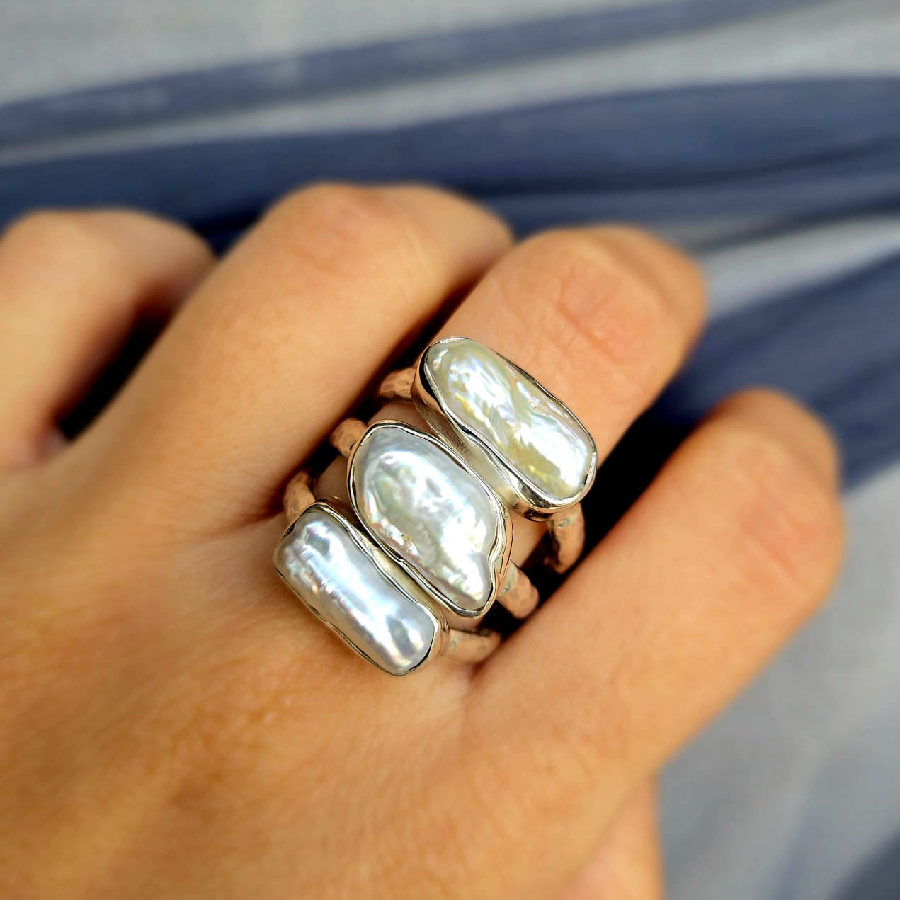 Hand wearing two pearl rings on a blurred background