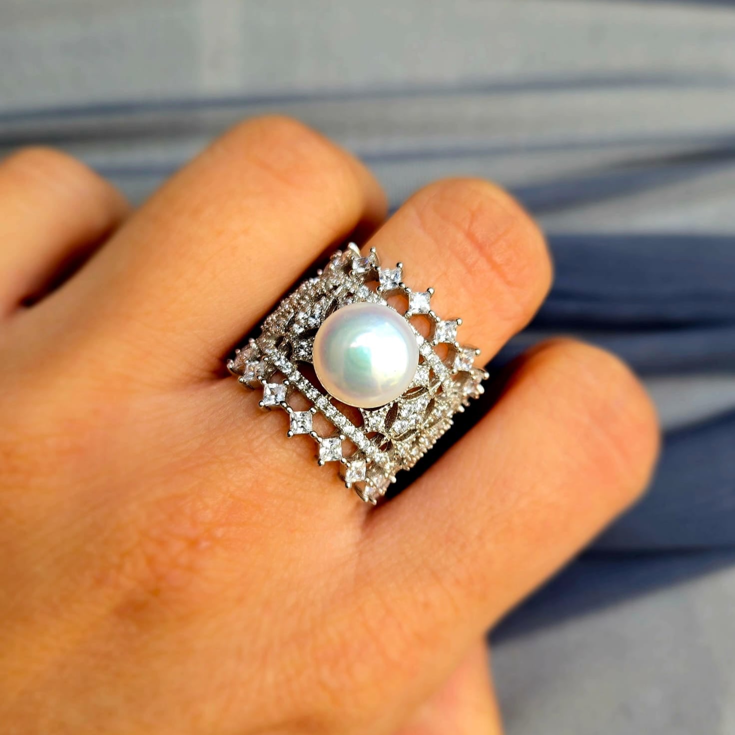 Pearl ring with diamond accents on a finger against a blurred background
