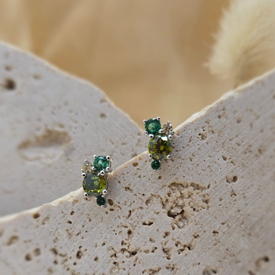 Pair of green gemstone earrings on a textured beige surface