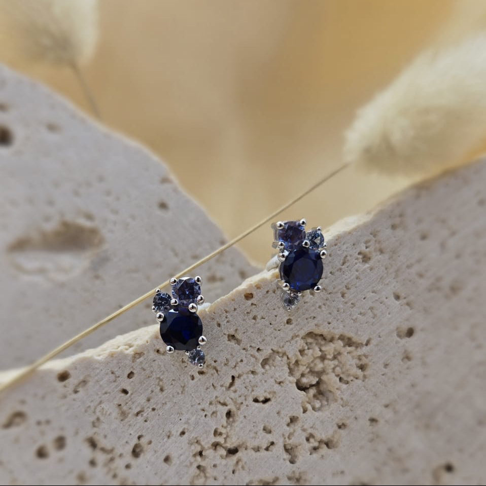 Pair of sapphire earrings on a textured stone surface with a blurred natural background