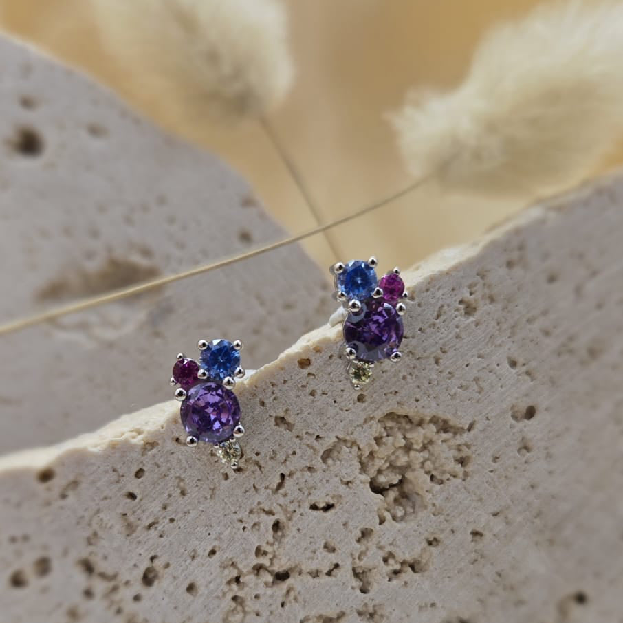 Pair of gemstone earrings on a textured surface with a blurred natural background