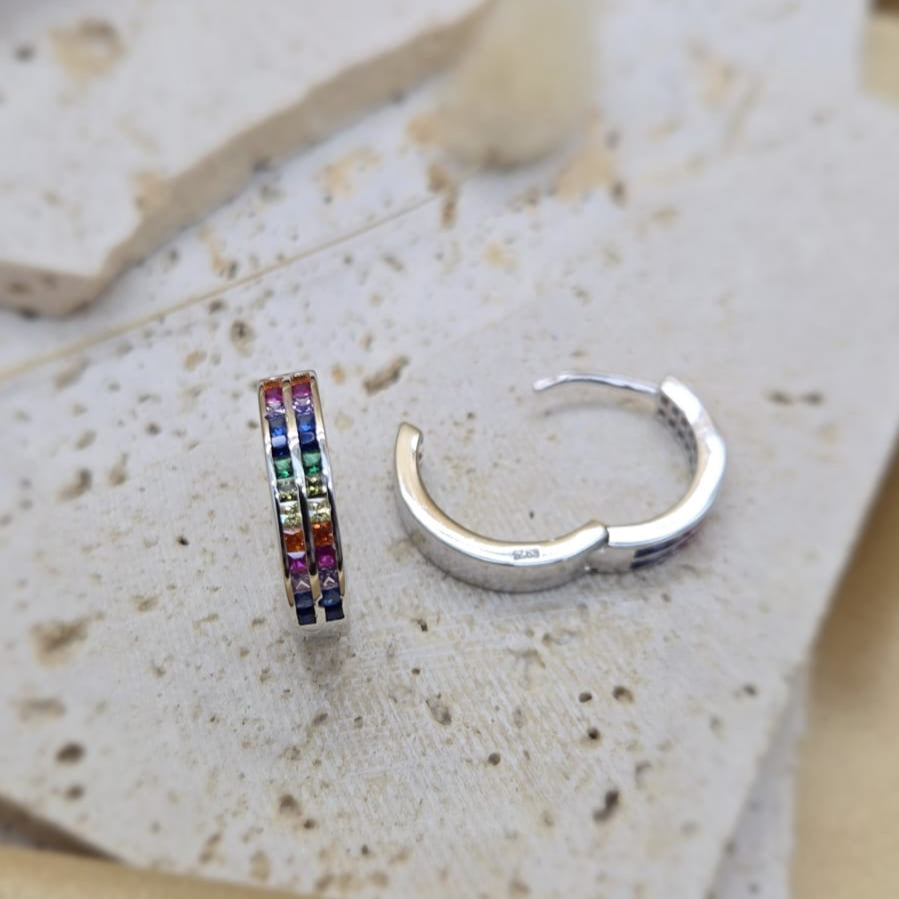 Silver hoop earring with colorful stones on a textured stone surface