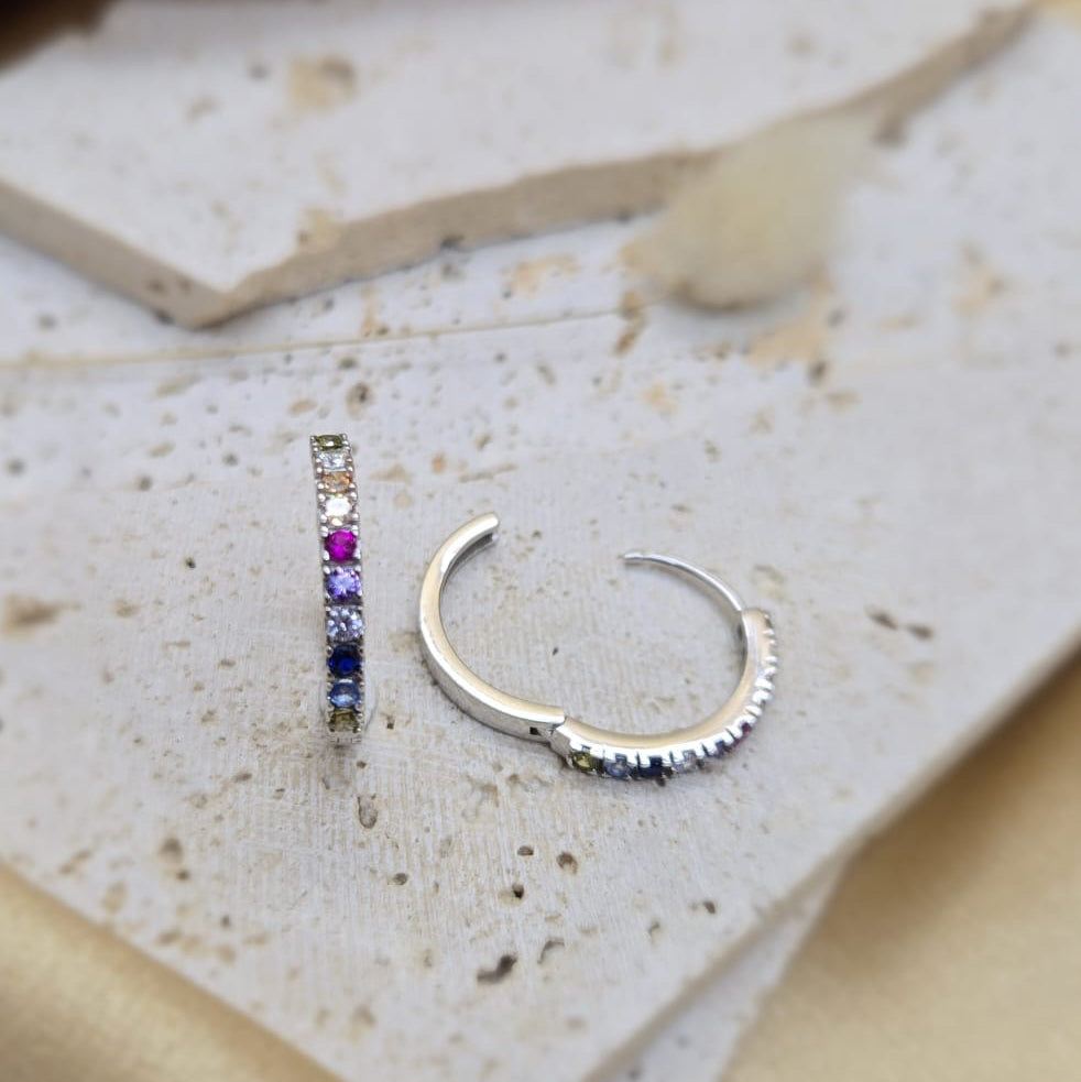 Silver hoop earrings with embedded gemstones on a textured surface