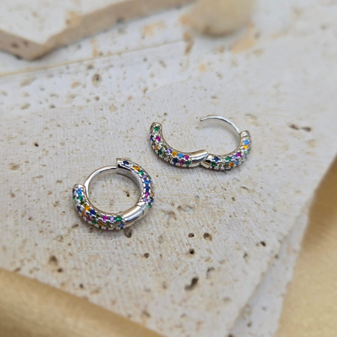 Silver hoop earrings with colorful gemstones on a textured stone surface