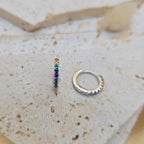 Small hoop earrings with colorful gemstones and silver finish on a textured surface