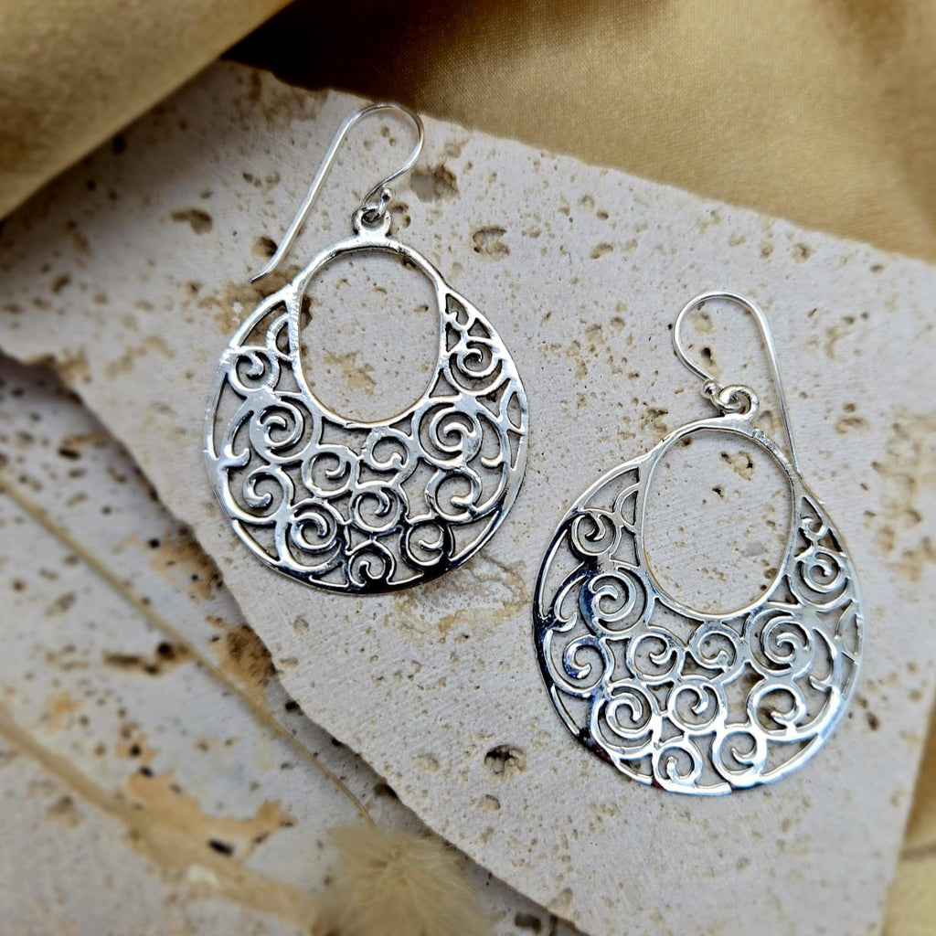 Silver earrings with intricate designs on a textured stone surface