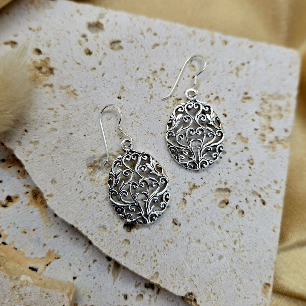 Silver filigree earrings on a textured beige card