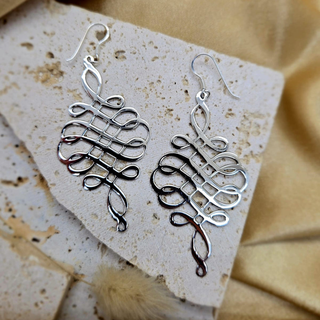 Silver earrings on a textured stone surface with a beige fabric background