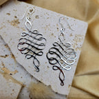 Silver earrings on a textured stone surface with a beige fabric background