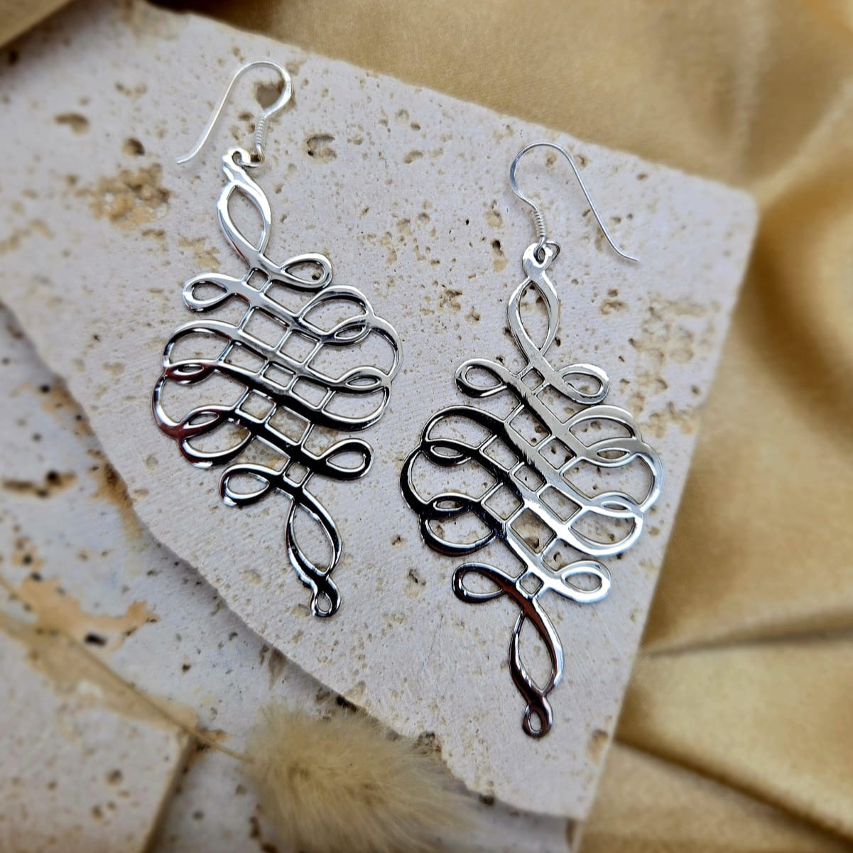 Silver earrings on a textured stone surface with a beige fabric background