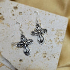 Silver cross earrings on a textured stone surface