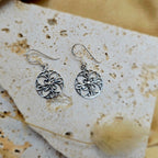 Silver floral earrings on a textured stone surface