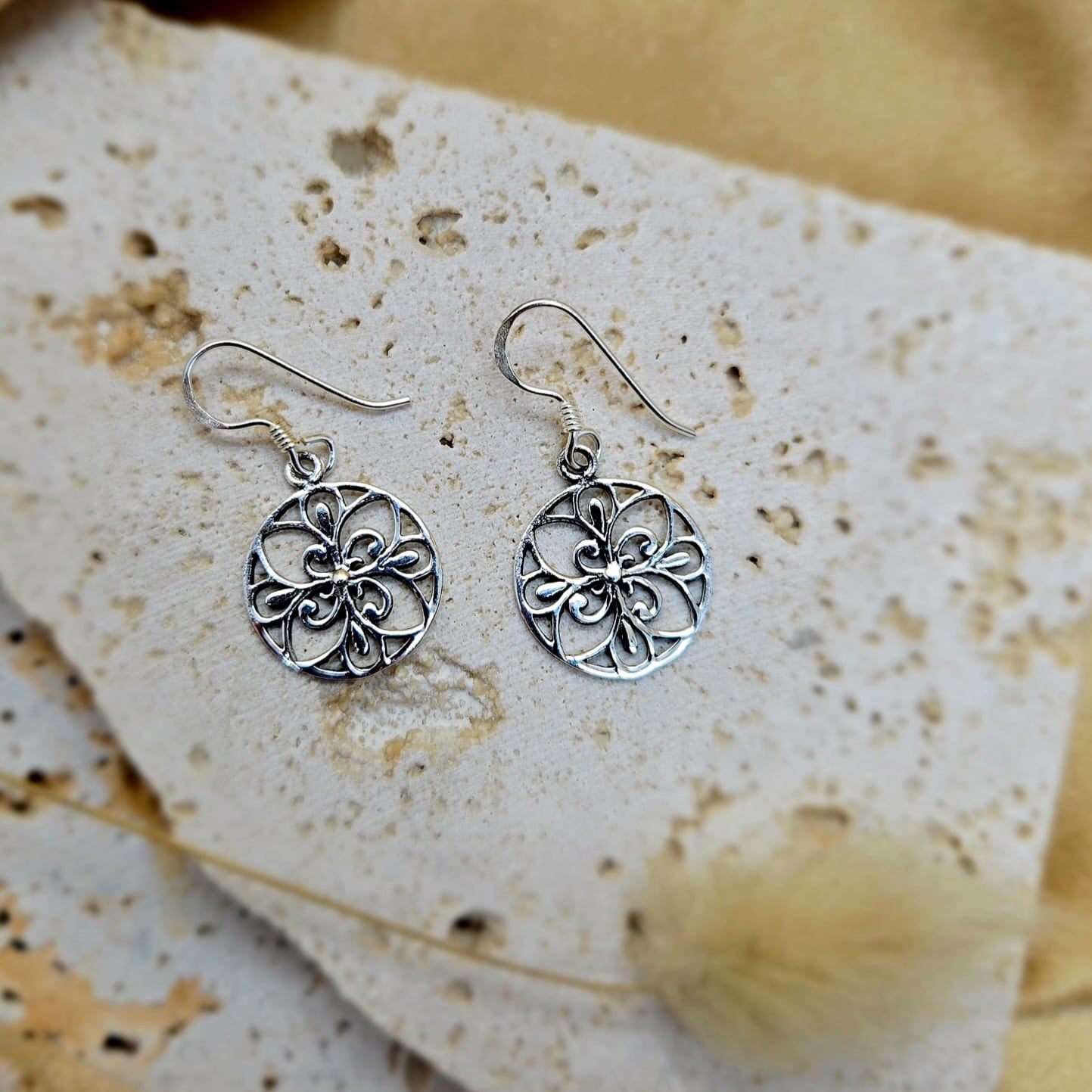 Silver floral earrings on a textured stone surface