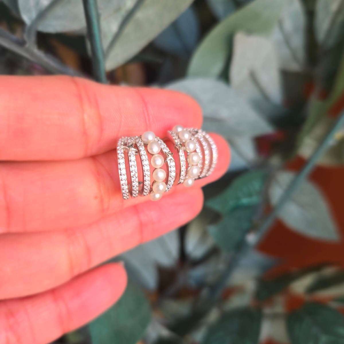 Silver ring with pearls held between fingers against a leafy background