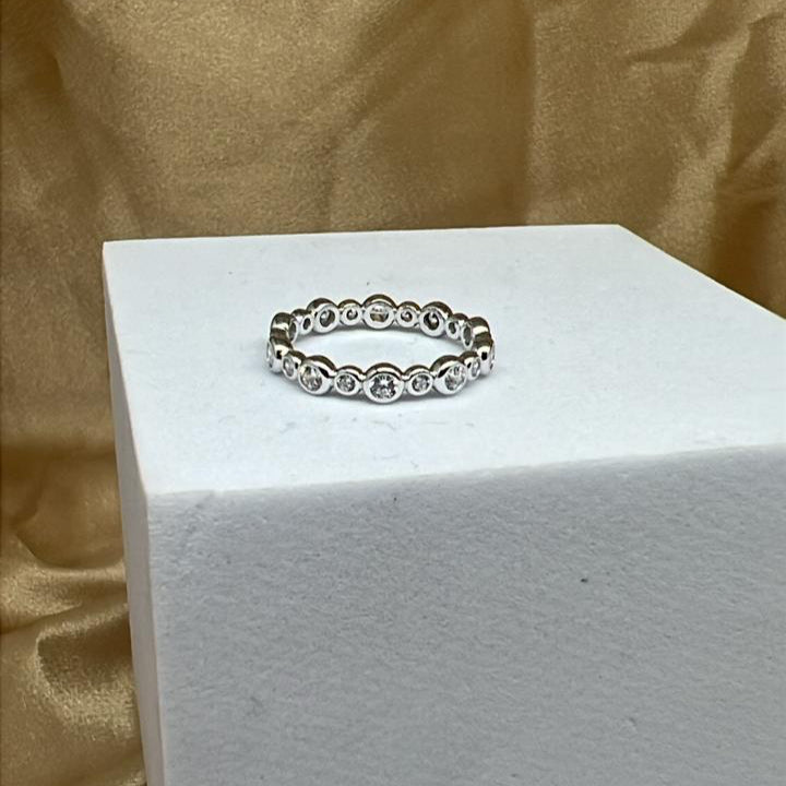 Silver ring with diamonds on a white stand against a gold fabric background