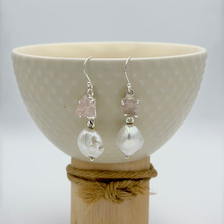 Pair of earrings with clear and pink gemstones displayed on a white bowl.
