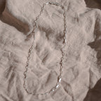 Silver chain necklace on a textured beige surface