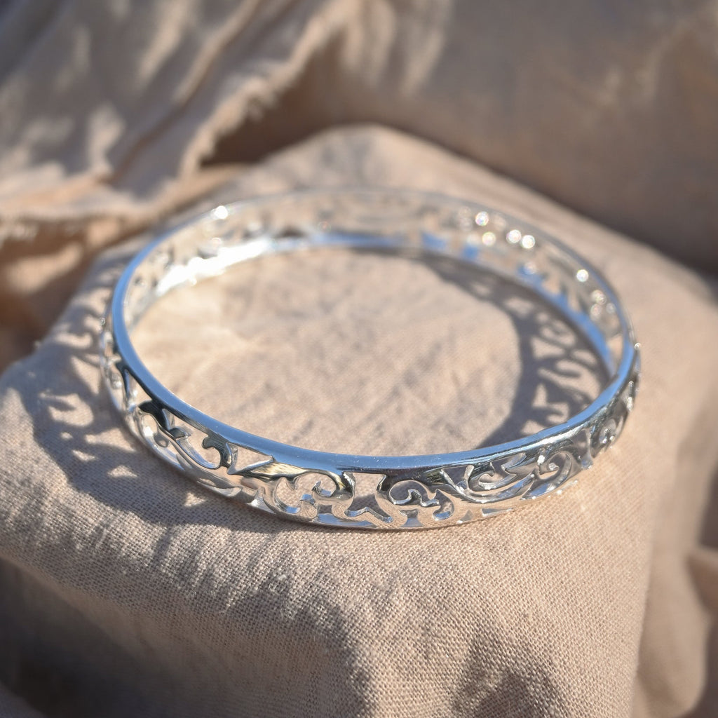 Silver bracelet with intricate design on a beige fabric background