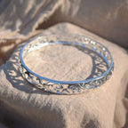 Silver bracelet with intricate design on a beige fabric background