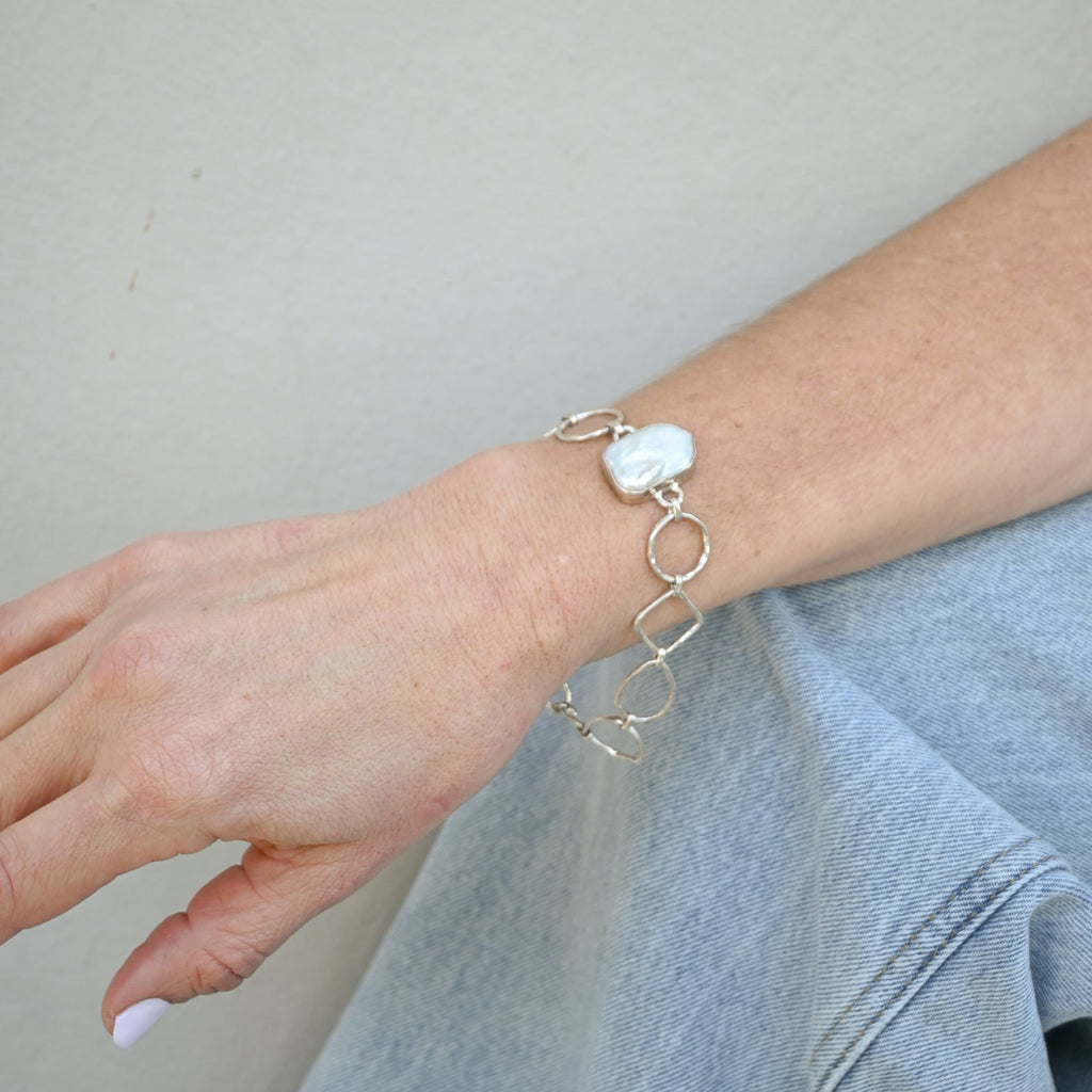 Silver bracelet with a large pearl on a wrist against a neutral background