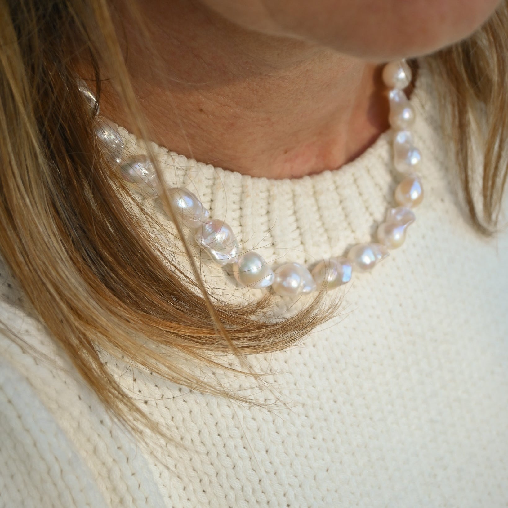 Close-up of a pearl necklace worn by a person with blonde hair.