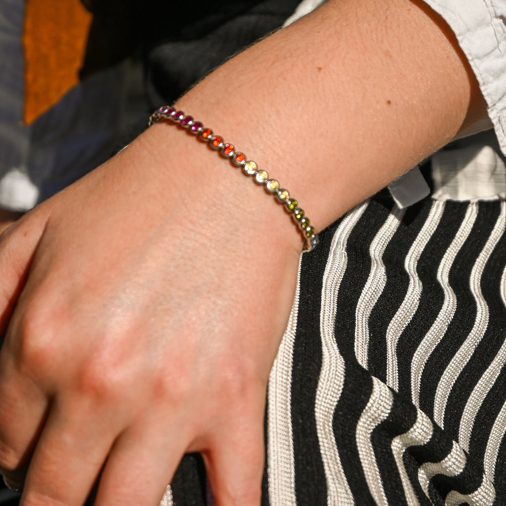 Close-up of a hand wearing a colorful beaded bracelet with a blurred background.