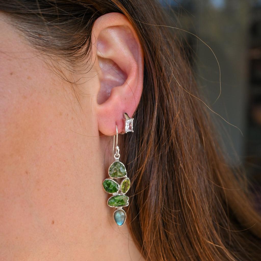 Close-up of a person wearing a silver earring with green and blue stones.