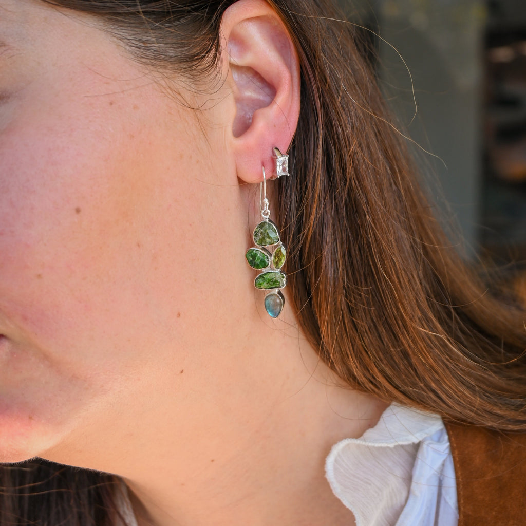 Close-up of a person wearing green leaf-shaped earrings with a blurred background