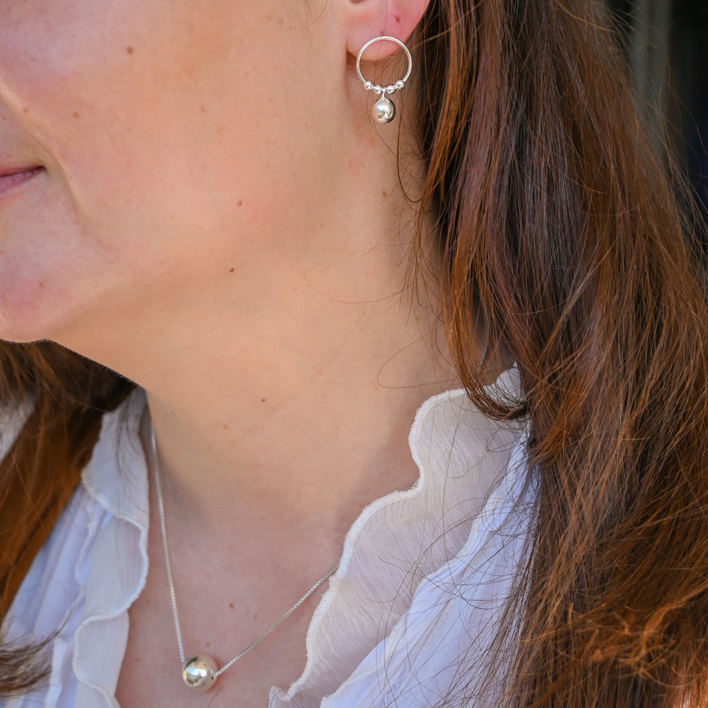 Close-up of a person wearing silver hoop earrings and a necklace with a white background.