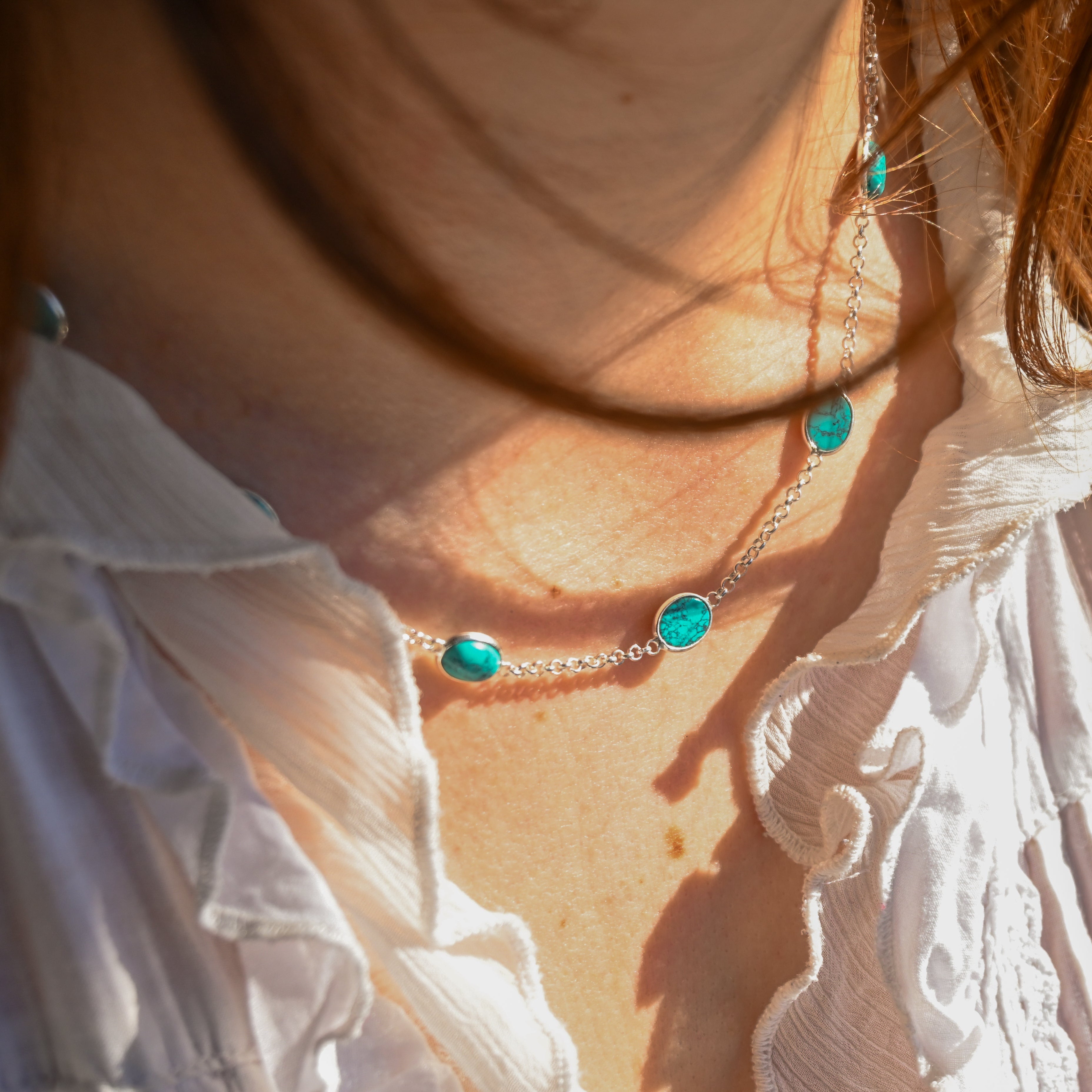 Close-up of a person wearing a necklace with turquoise stones, sunlight casting shadows.