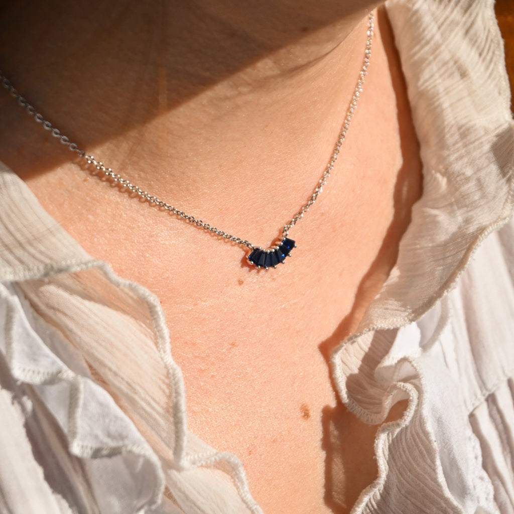 Necklace with a blue pendant worn by a person in a white blouse.