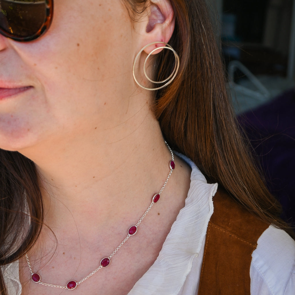 Close-up of a person wearing sunglasses, hoop earrings, and a necklace with red beads.