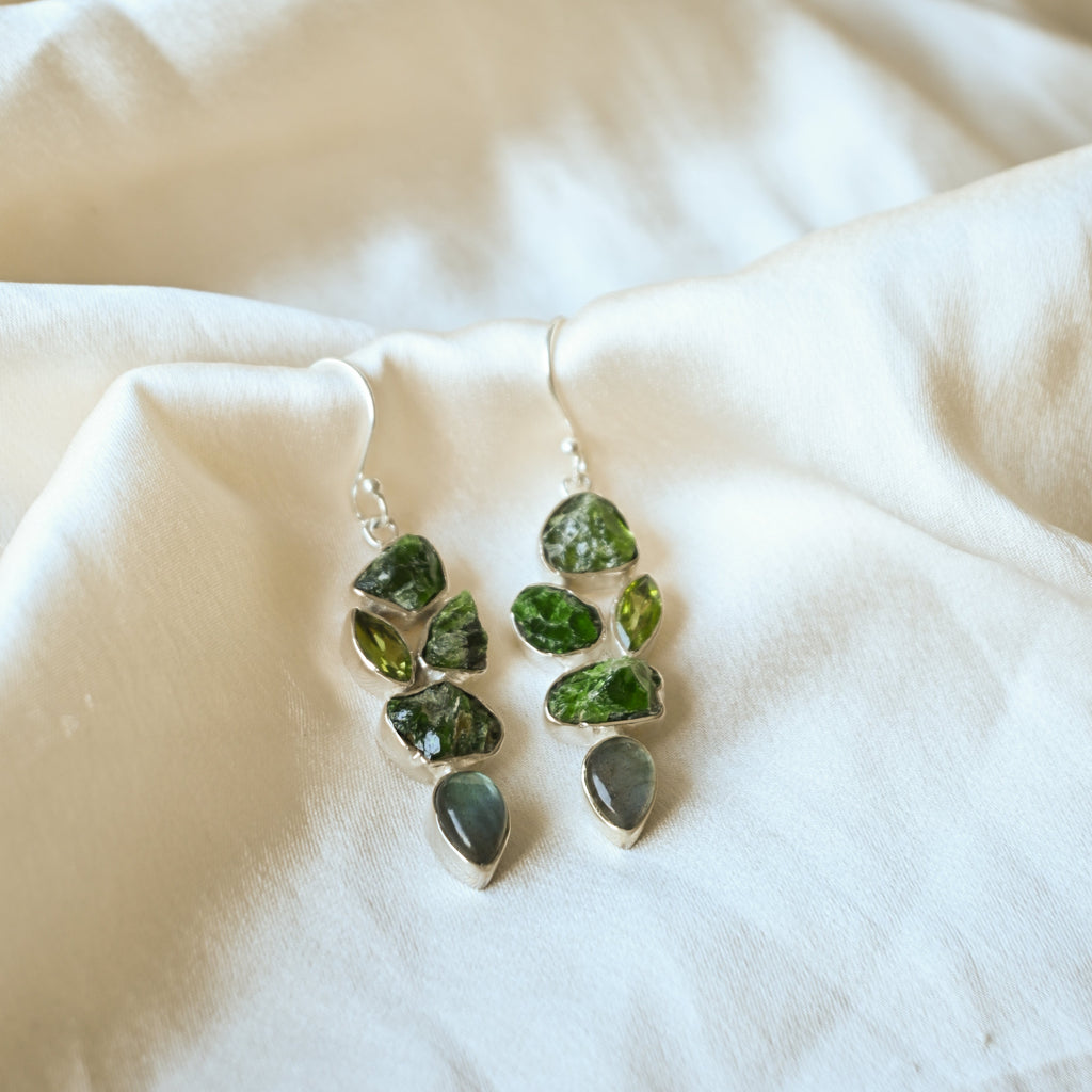 Green leaf-shaped earrings on a white fabric background