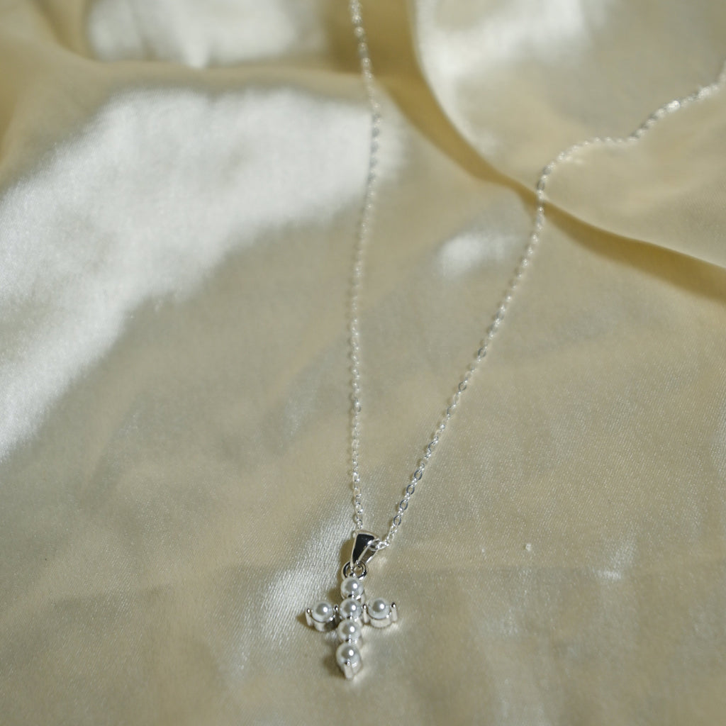 Silver cross necklace on a beige fabric background
