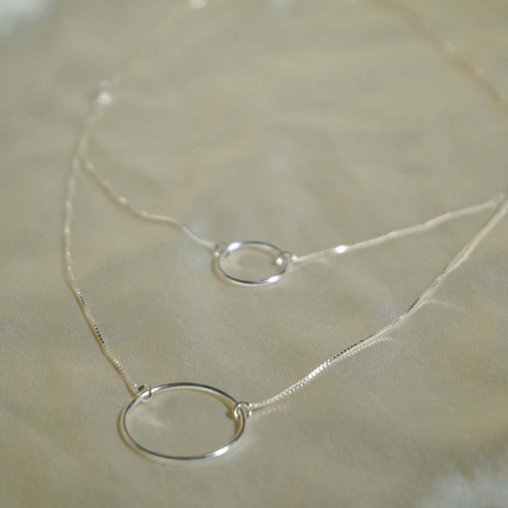 Silver necklace with a simple ring pendant on a beige fabric background