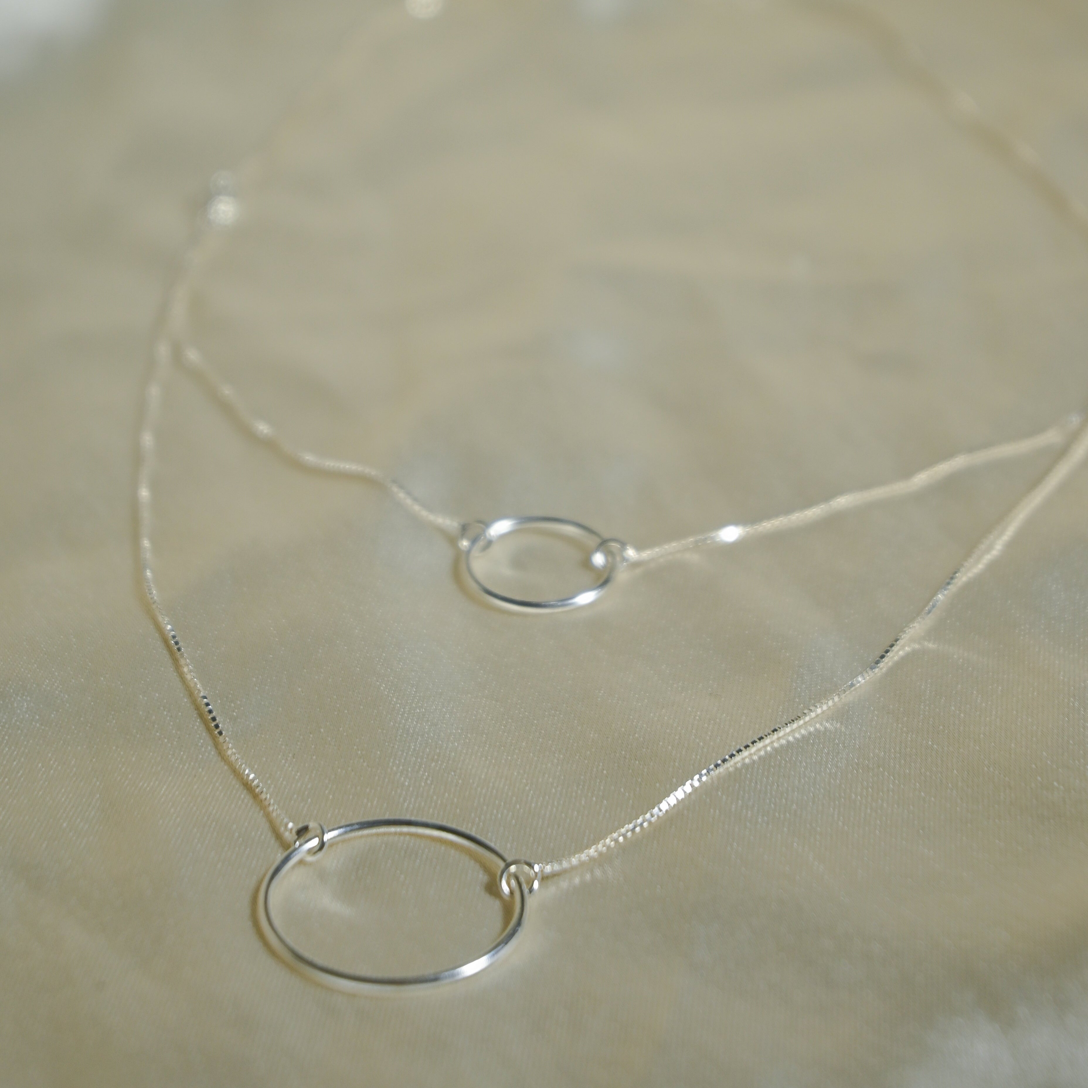 Silver necklace with a simple ring pendant on a beige fabric background